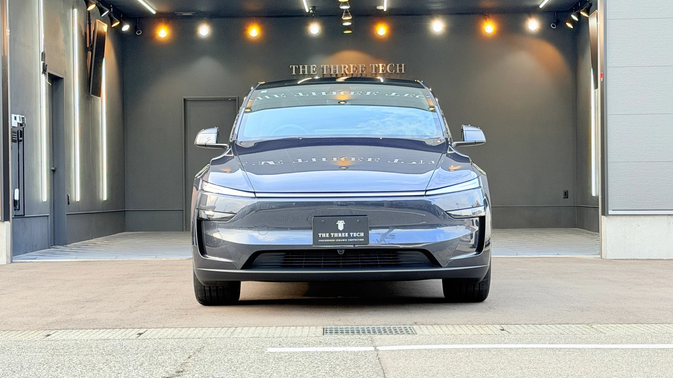 石川県小松市のTHE THREE TECH施工スタジオ前で撮影した、FEYNLAB CERAMIC ULTRA Ver.3施工後のテスラ Model Y・ステルスグレーのフロント正面写真